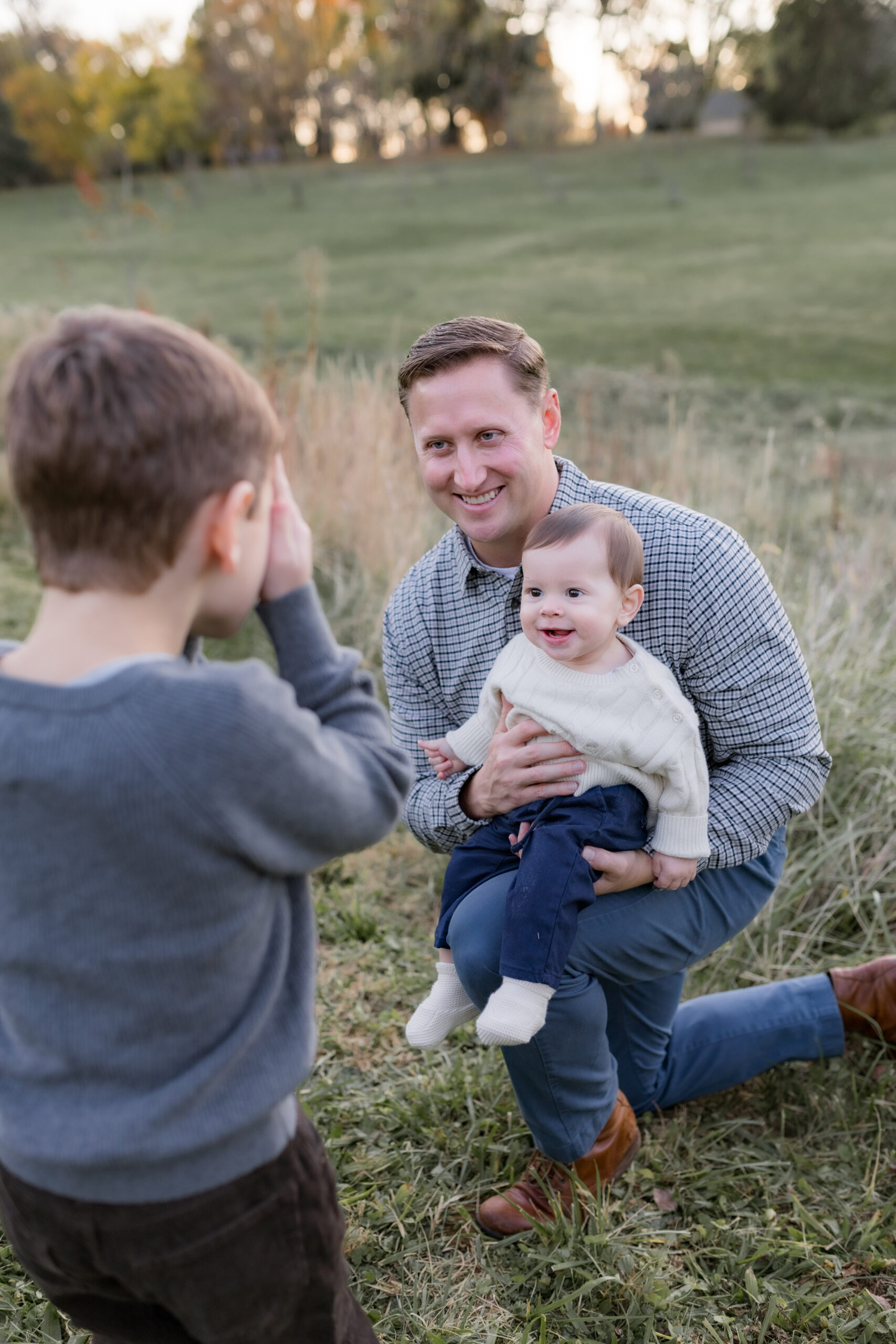 dad holding baby playing peek a boo with older son for family photo session in louisville ky