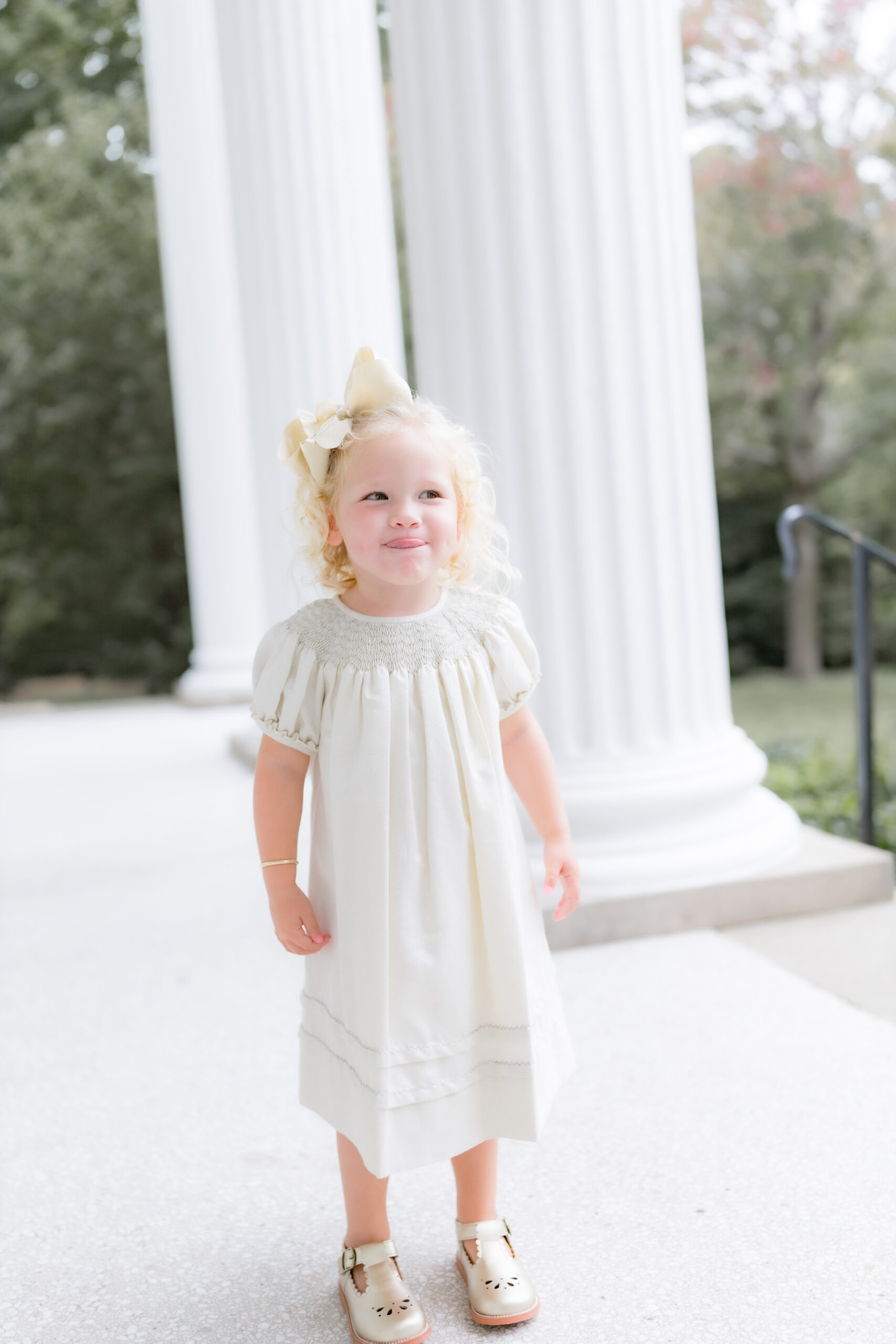little girl in light colored clothes sticking tongue out smiling